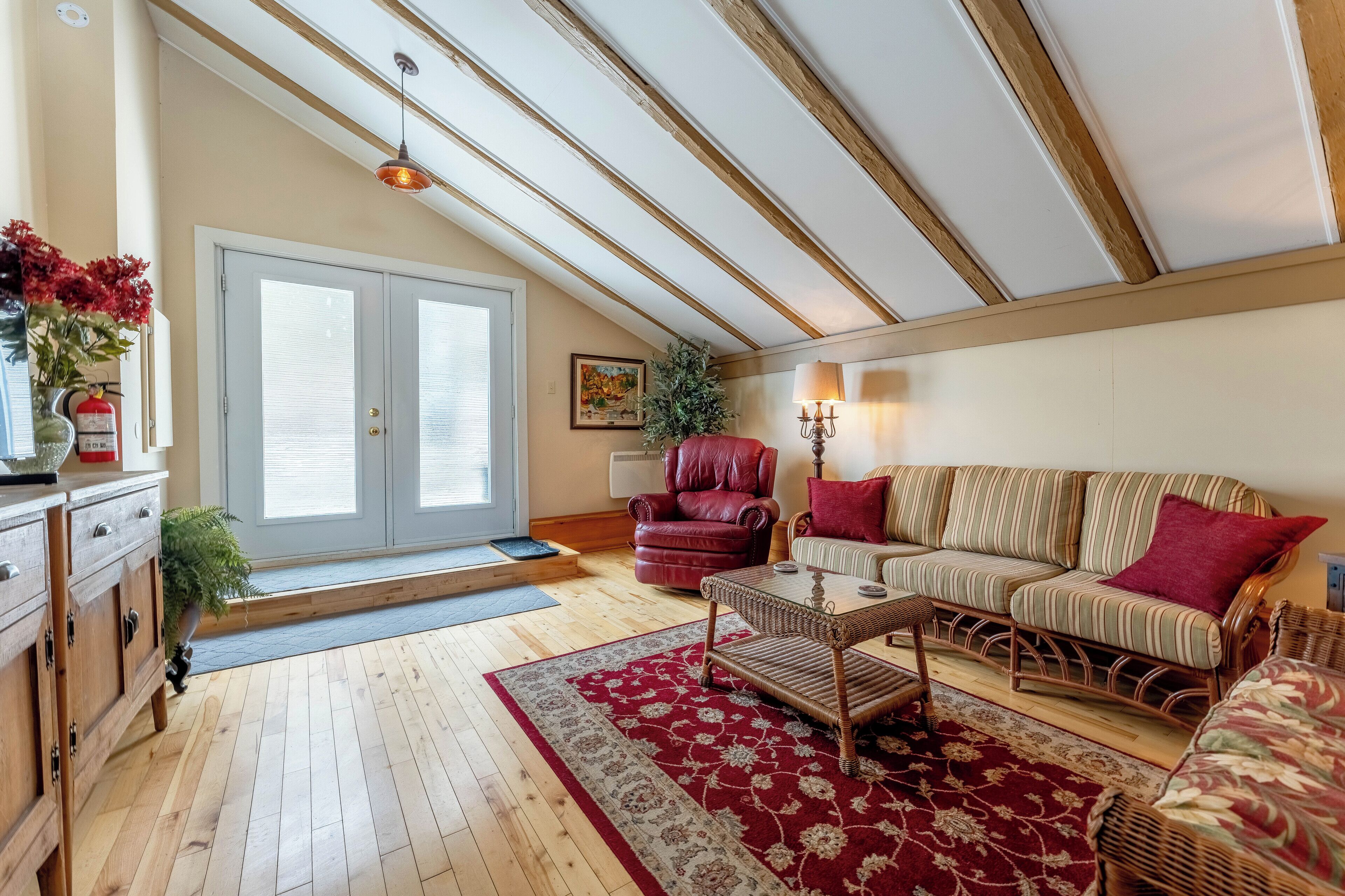 A cozy living room with a wooden floor, a striped sofa, a red armchair, and a coffee table.