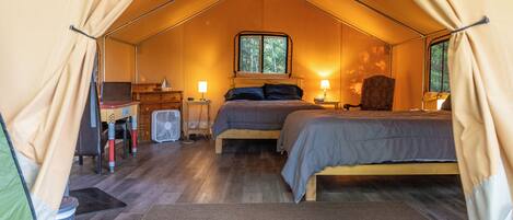 A tented accommodation with a bed, bedside table, lamp, and a window.