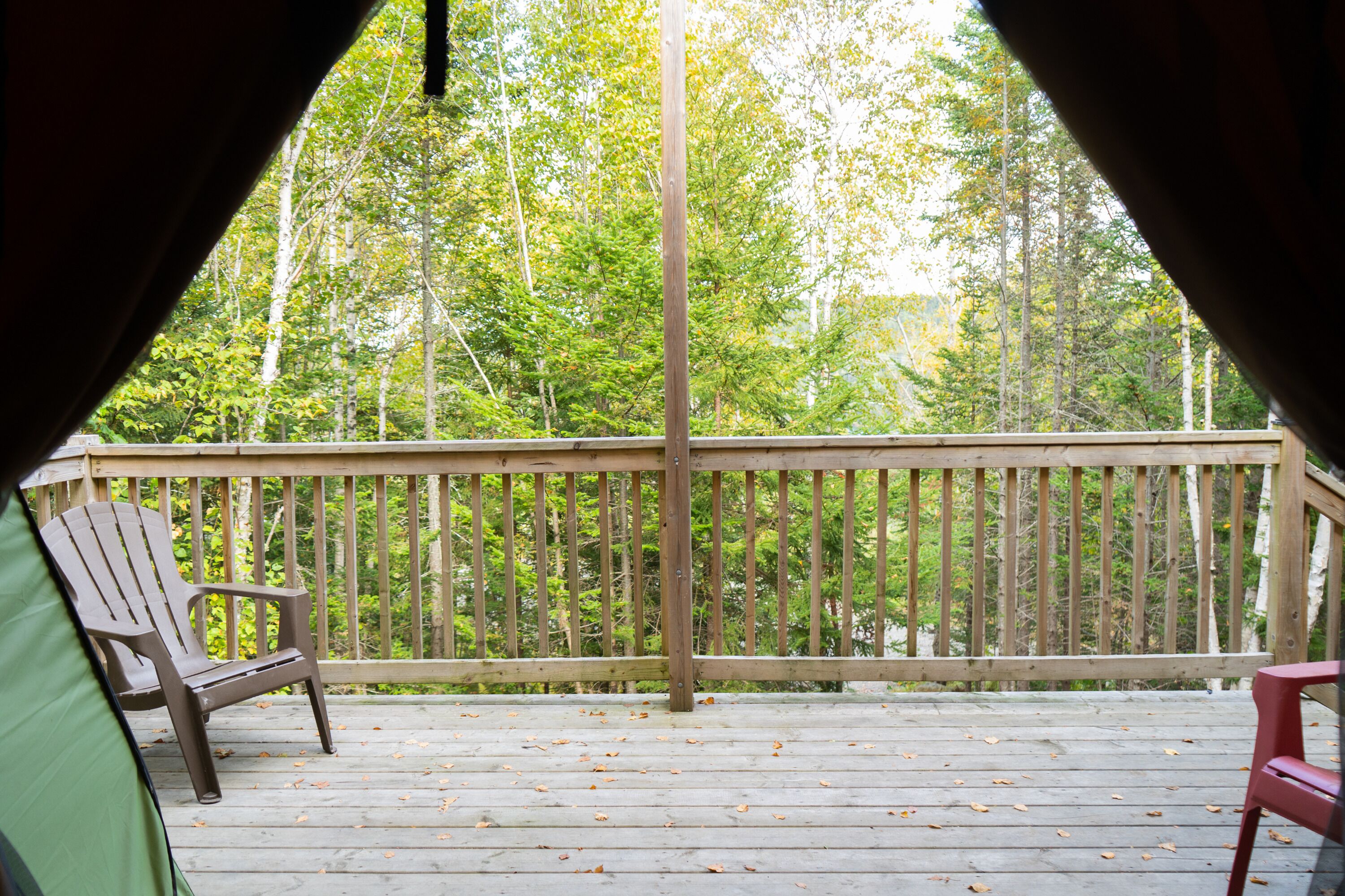 A wooden deck with a railing, a green tent, and two chairs.