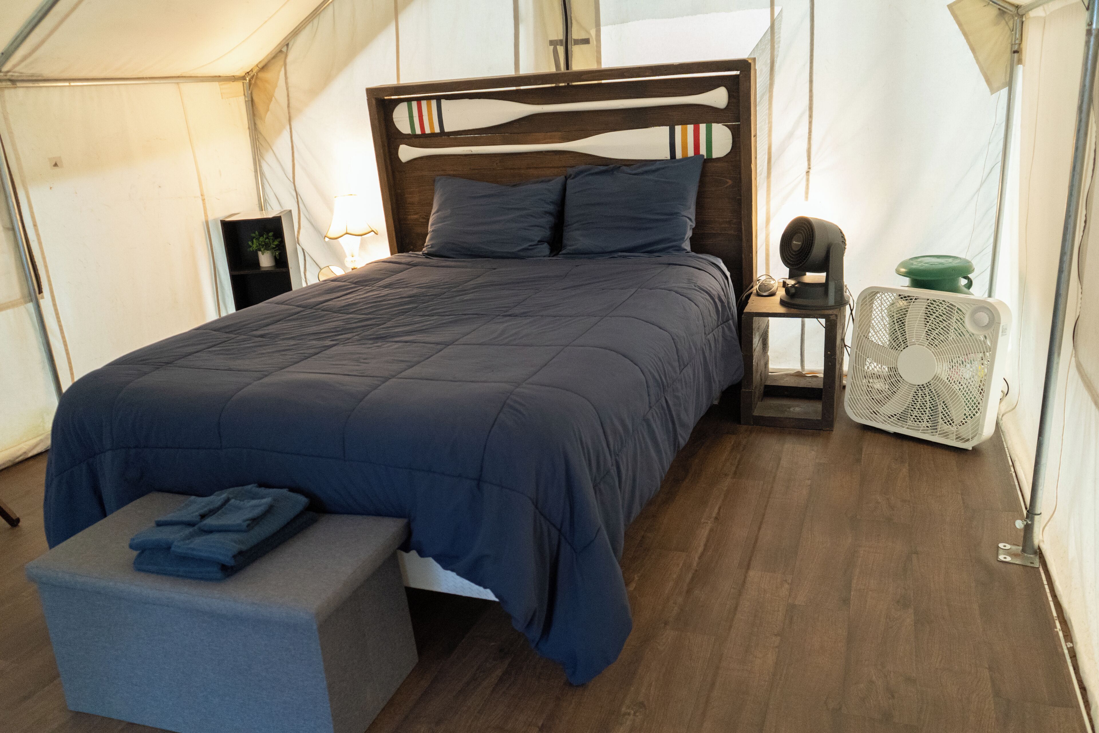 Una habitación con carpa, una cama, una mesita de noche, un ventilador y un banco.