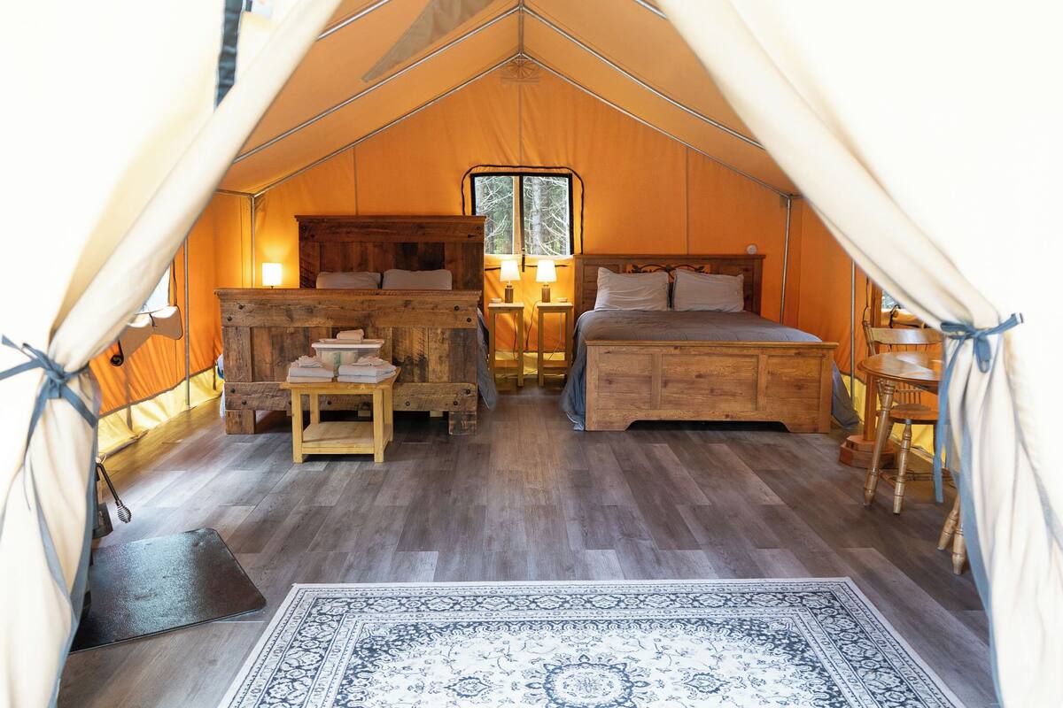 A tented accommodation with a bed, bedside tables, a window, and a rug.