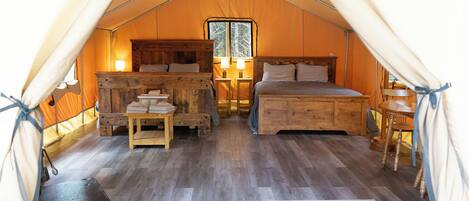 A tented accommodation with a bed, bedside tables, a window, and a rug.