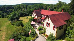 A two-story house with a red roof, surrounded by a lush green landscape and trees. - Dominion Hill Country Inn (Digdeguash)