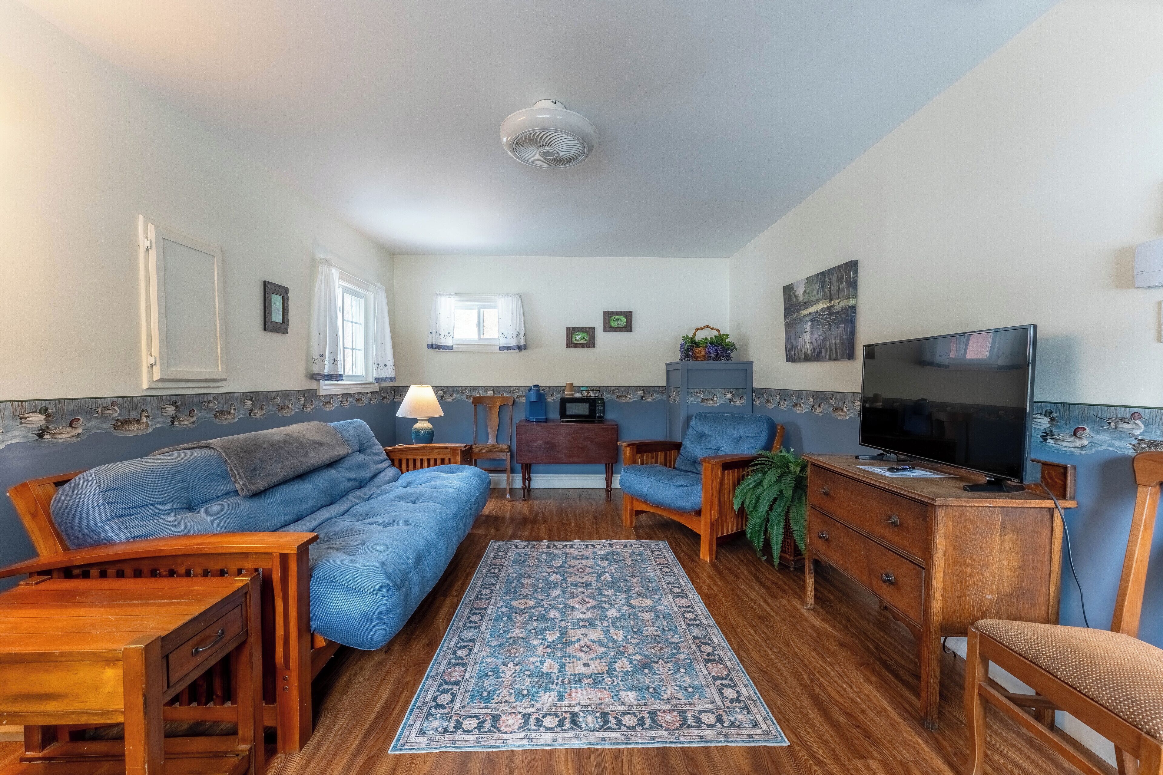 A cozy living room with a sofa, armchairs, a TV, and a wooden cabinet.