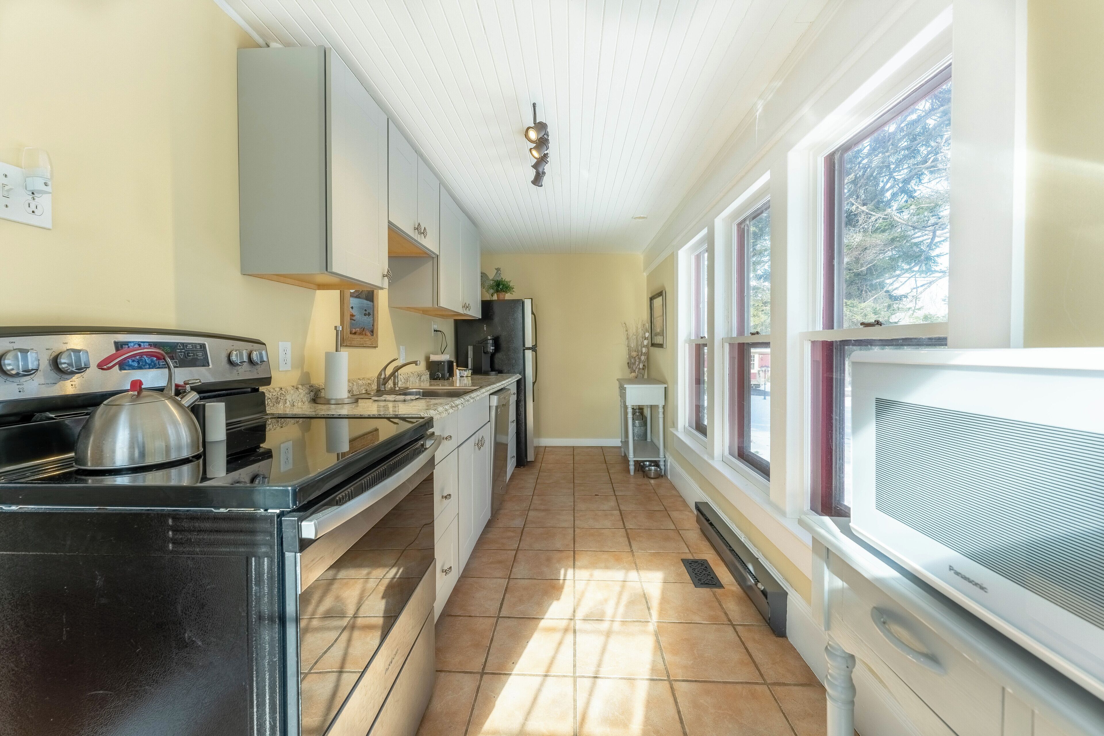 A kitchen with a stove, oven, microwave, and refrigerator. There are cabinets, a sink, and a window with a view of trees.