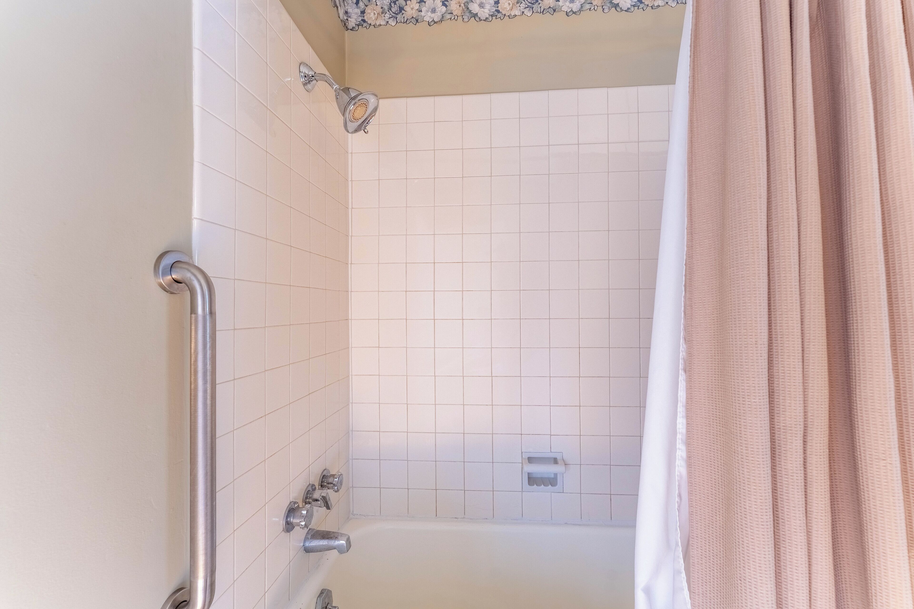 A bathroom with a bathtub, a shower, and a handrail.