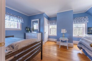 Un dormitorio con una cama de madera, un tocador, una cómoda y dos ventanas con cortinas decoradas con motivos florales.