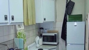 A compact kitchen with white cabinets, a microwave, a stove, and a refrigerator. - Harare City 1-bed Apartment (Harare)