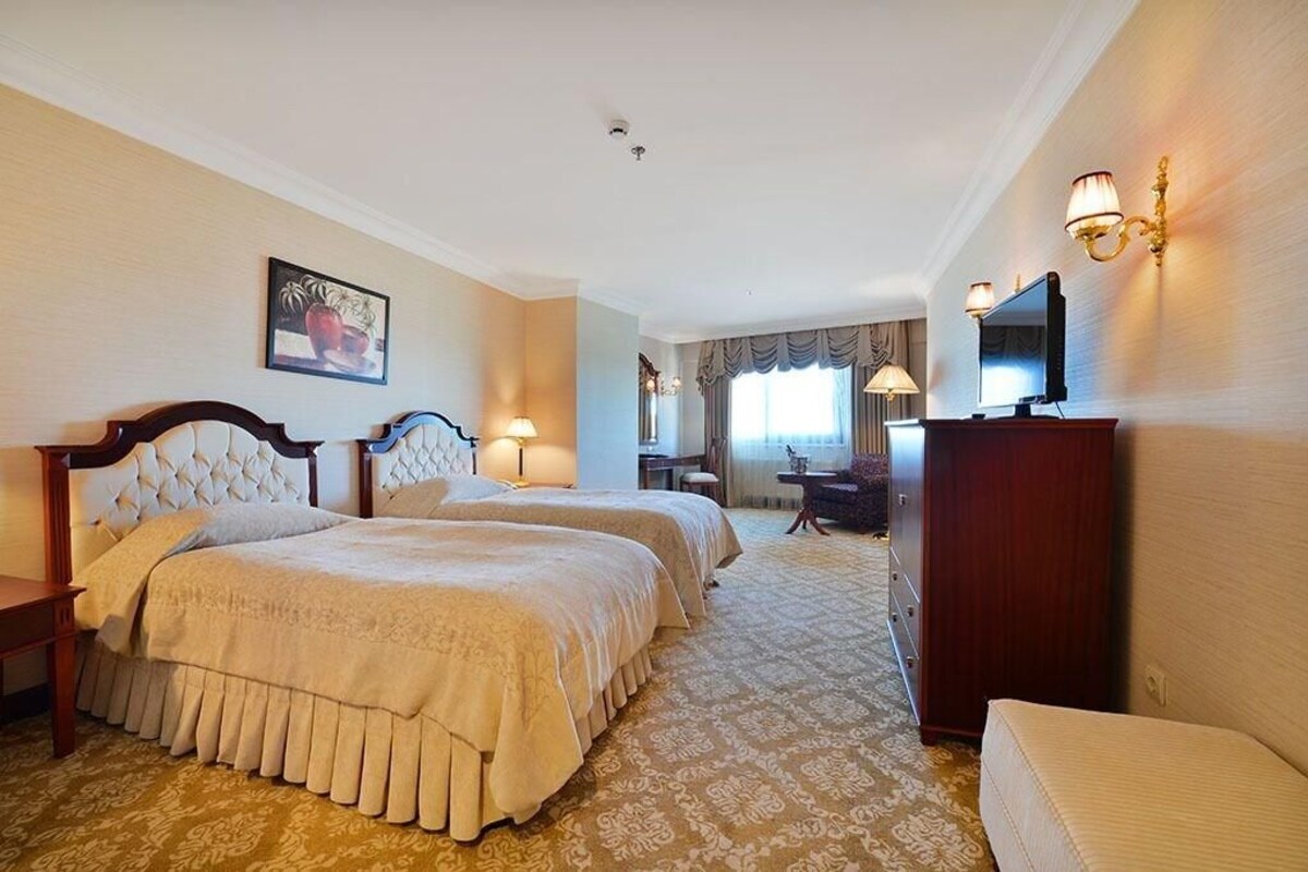A hotel room with two beds, a desk, a chair, a television, and a decorative wall piece.