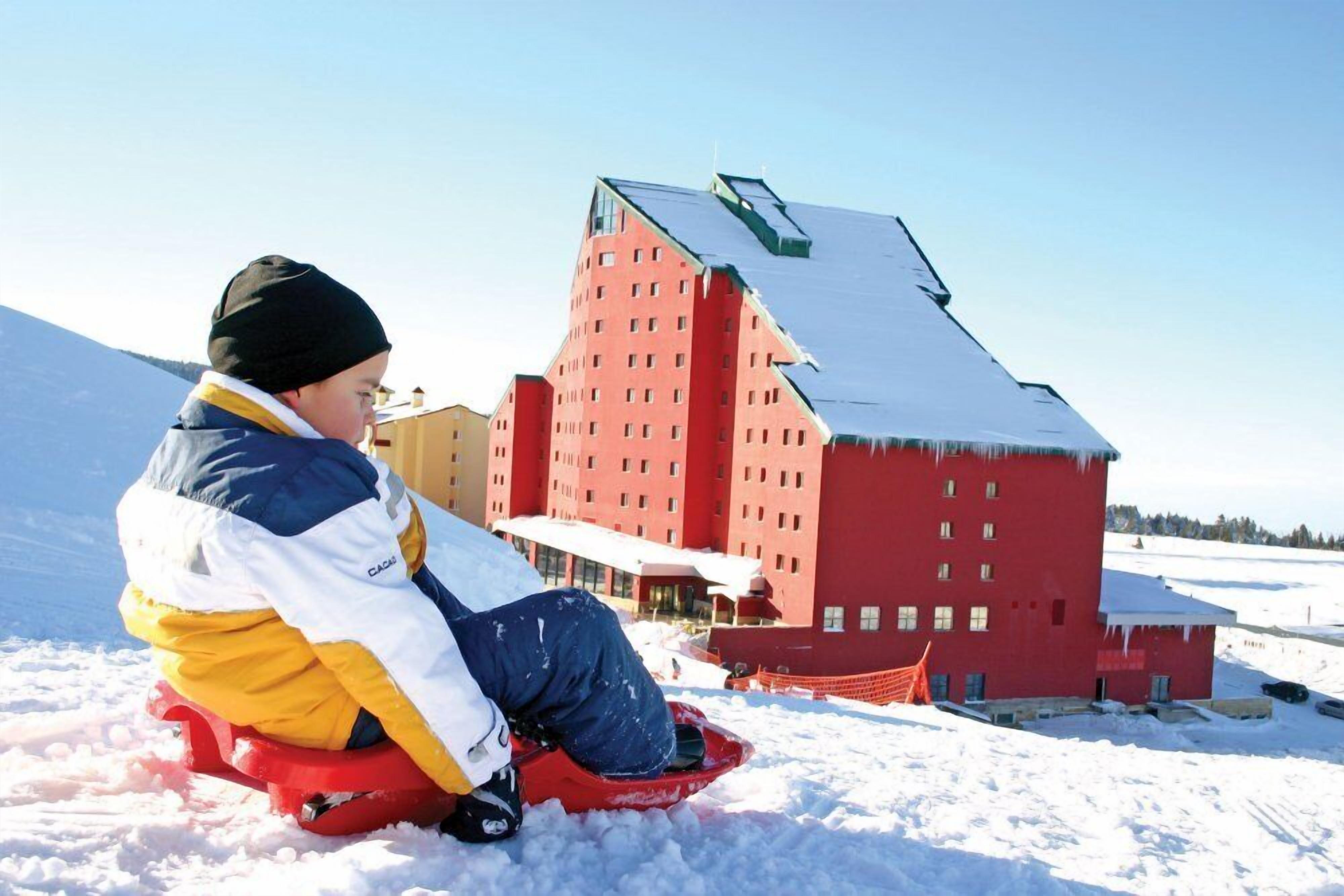 A person sledding on a red sled in a snowy landscape with a red building in the background.
