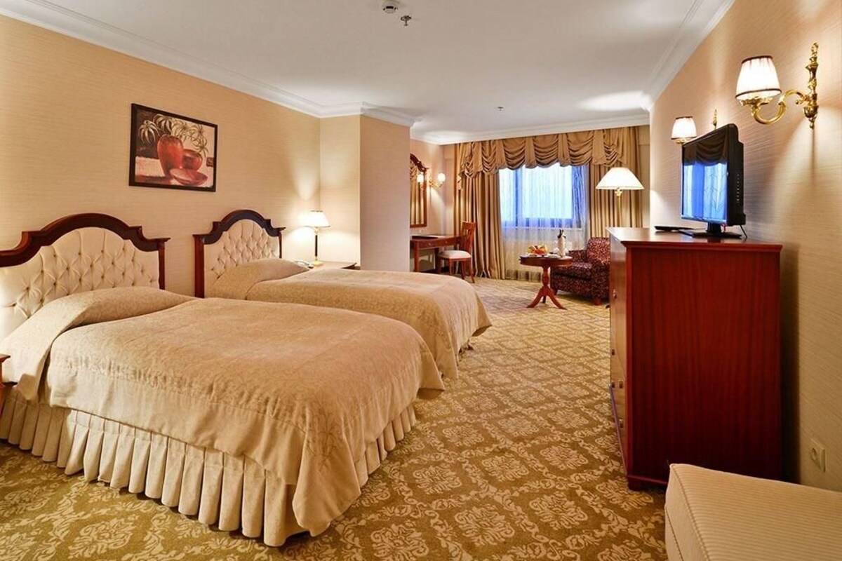 Habitación de hotel con dos camas, un escritorio, televisión y zona de comedor con cortinas.