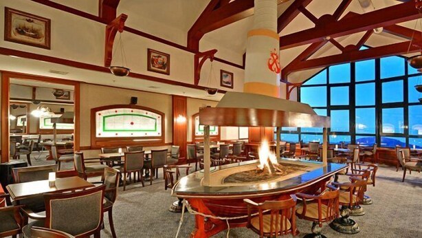 A restaurant with a central fire feature, tables, chairs, and large windows offering a view. - Karinna Hotel Uludag (Bursa)