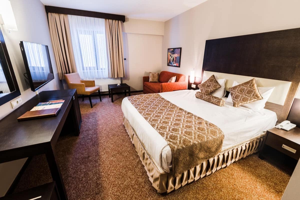 Une chambre d’hôtel avec un grand lit, un bureau avec un ordinateur, une chaise, un canapé et une télévision.