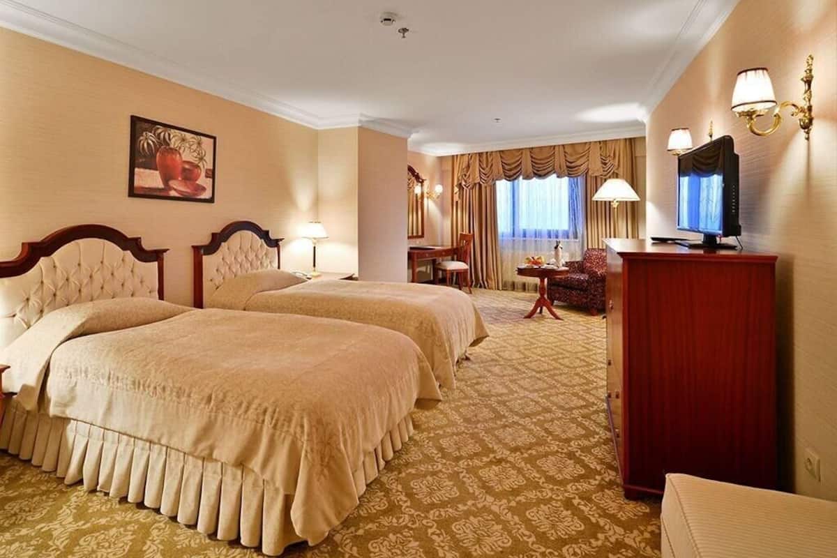 Une chambre d’hôtel avec deux lits, un bureau, une télévision et un coin repas agrémenté de rideaux.