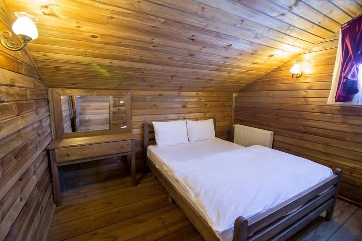 Un dormitorio de cabaña de madera con una cama individual, una mesita de noche y una lámpara fijada a la pared.