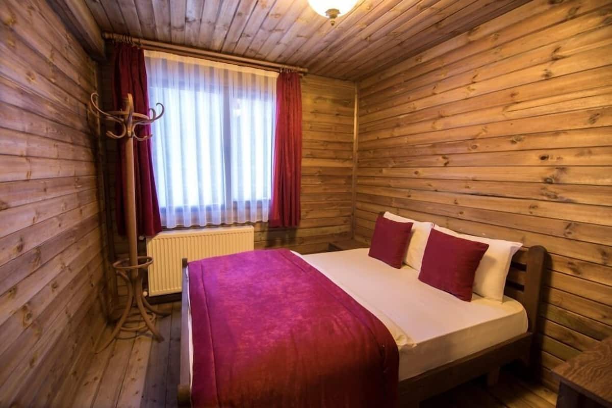 Habitación tipo cabaña de madera con cama, radiador y ventana con cortinas.