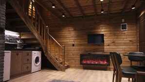A cozy cabin interior with a wooden staircase, a fireplace, a washing machine, and a television mounted on the wall. - Uludag Orman Koskleri (Bursa)