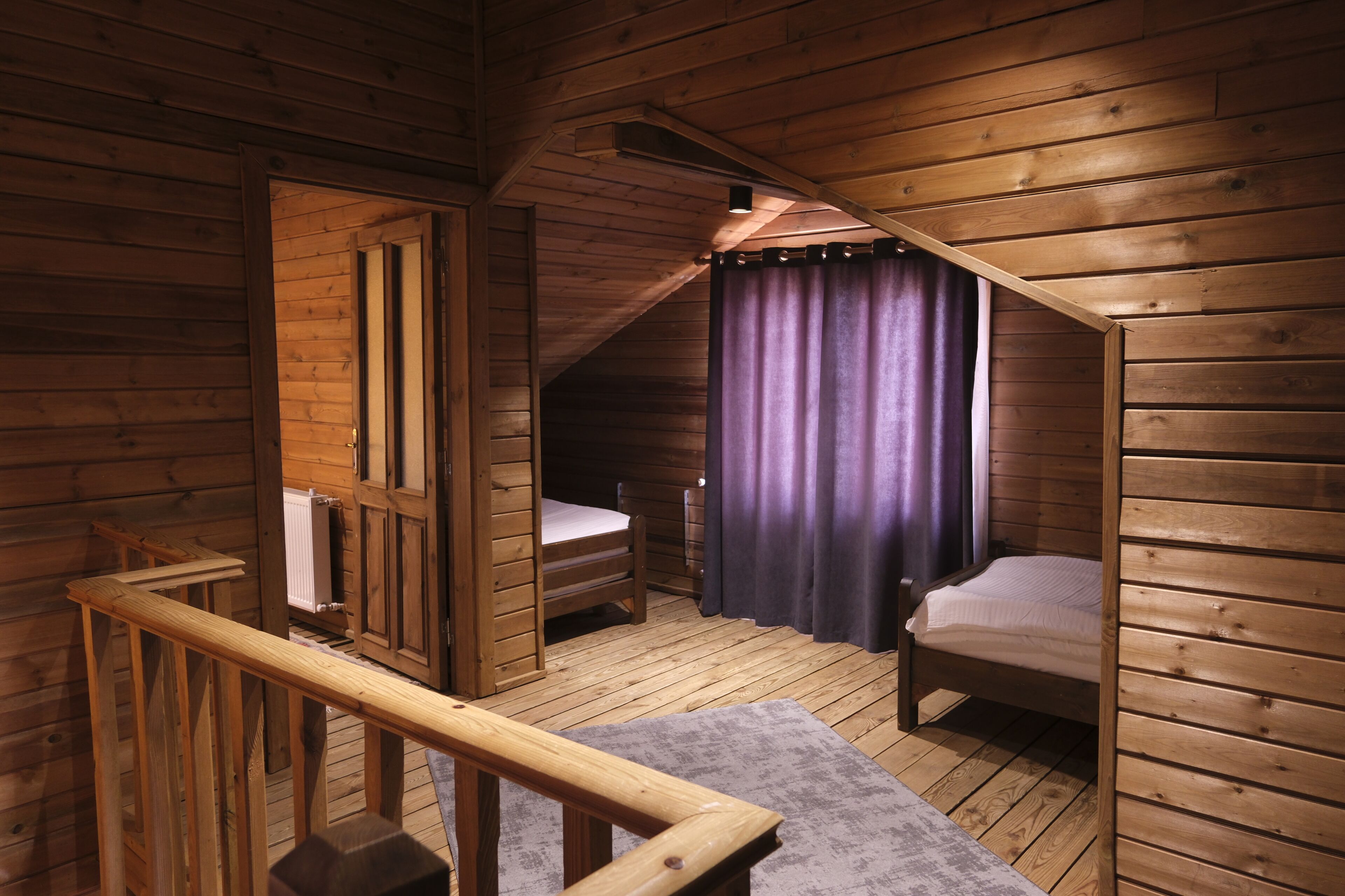 Una cabaña de madera con un dormitorio en el altillo, una escalera de madera y una ventana con cortinas.
