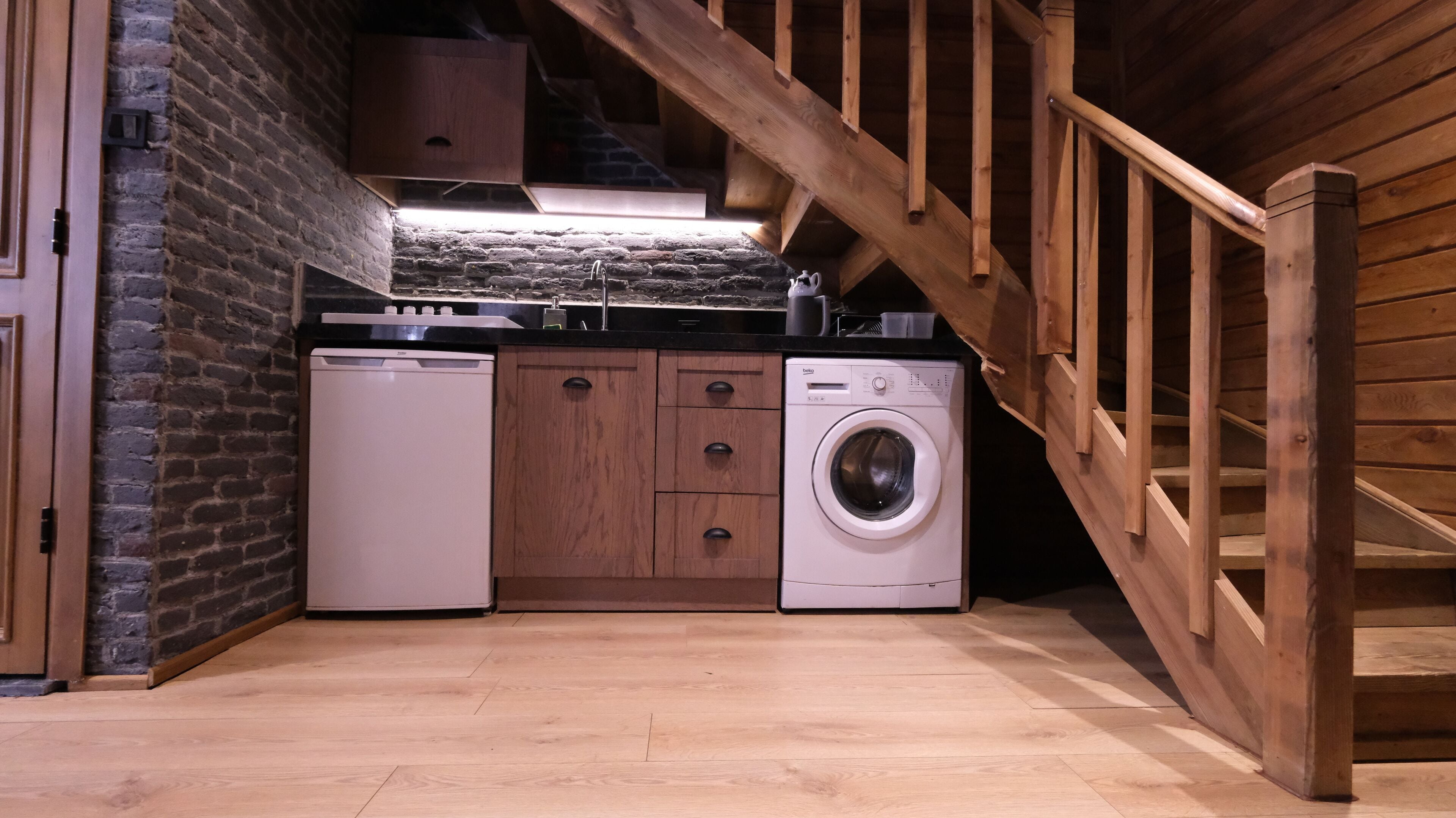 Une cuisine compacte équipée d’un lave-vaisselle, d’un lave-linge et de meubles de rangement en bois.