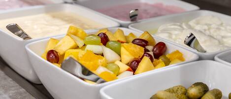 A buffet with various food items including fruits, cheeses, and pickles.