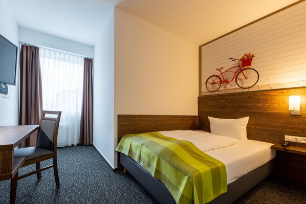 A hotel room with a bed, a desk, a chair, a window with curtains, and a wall-mounted bicycle. - Trip Inn Hotel Münster City (Münster)