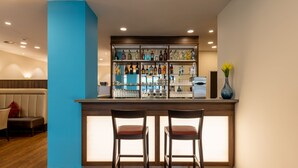 A bar area with a blue accent wall, wooden bar counter, and two bar stools. - Trip Inn Hotel Münster City (Münster)