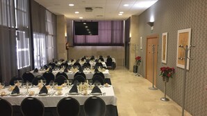 Une salle de conférence avec de longues tables disposées pour un événement formel, équipée de chaises, de tables et d’un grand écran à l’avant.