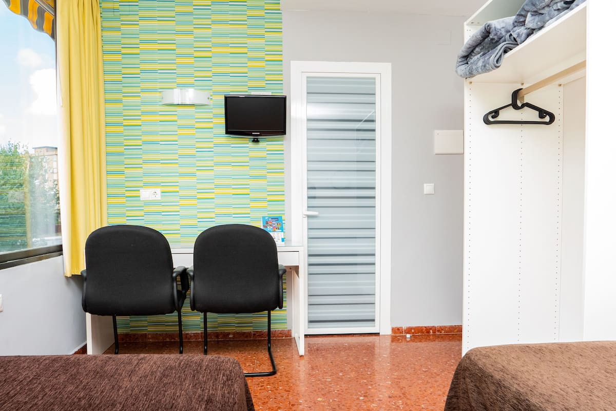 A room with a striped wall, a TV, a desk, two chairs, a wardrobe, and a window with curtains.