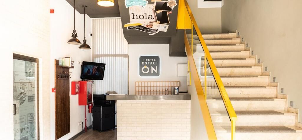 Una zona de recepción con mostrador, televisor y un cartel que dice "Hostal Estaci ON".