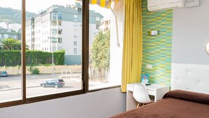 Une chambre d’hôtel avec un lit, un bureau et une fenêtre donnant sur une rue et des immeubles.