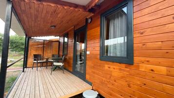 Una cabaña de madera con un porche cubierto, un comedor y una ventana con cortinas.