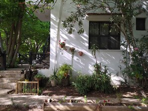 Una casa blanca con una escalera de madera que lleva a un porche, rodeada de macetas y árboles.