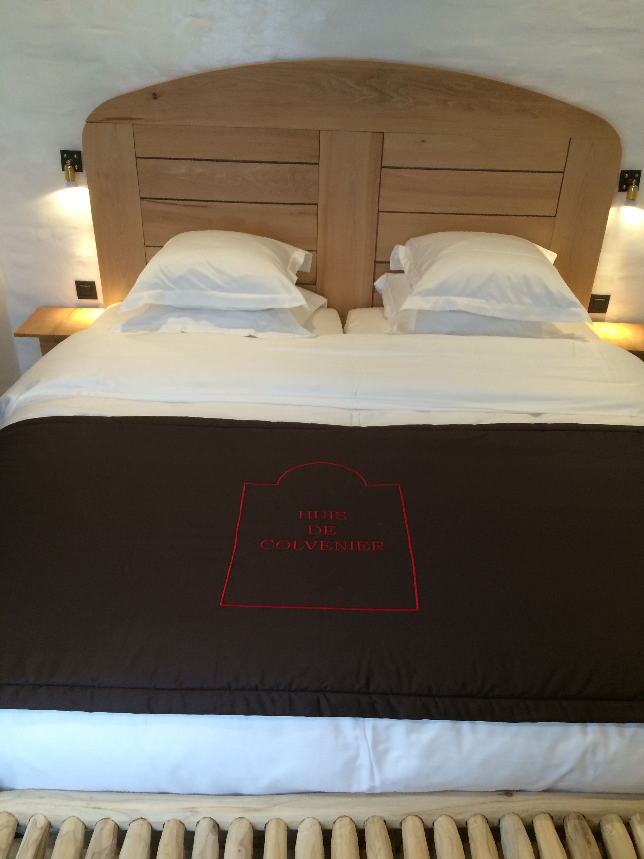 A bed with a wooden headboard, white bedding, and a black pillow with red text.