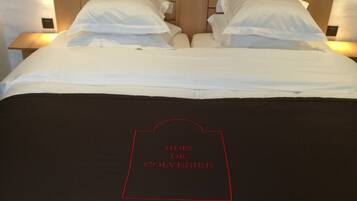 A bed with a wooden headboard, white bedding, and a black pillow with red text.