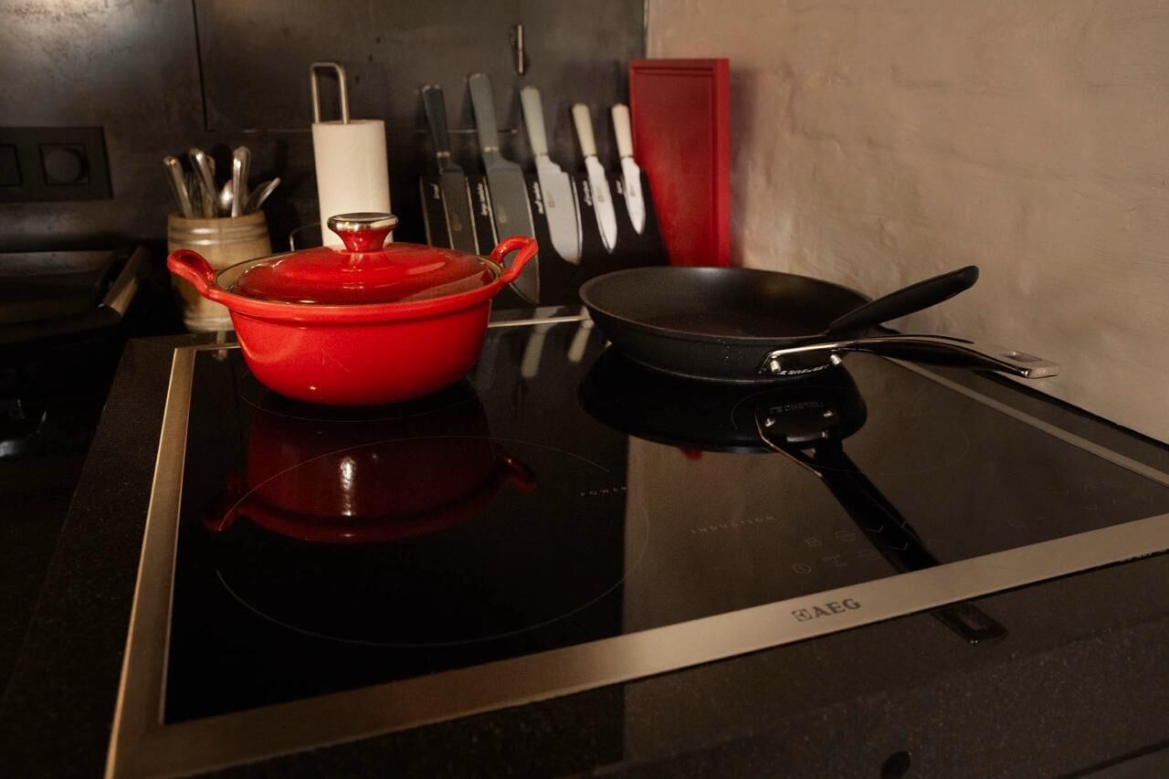 Una cocina con una olla roja sobre una cocina de inducción, una sartén negra y un bloque para cuchillos con varios cuchillos.