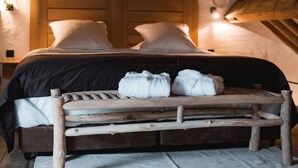Un dormitorio acogedor en el ático con una cama de madera, un banco con toallas y un techo inclinado.