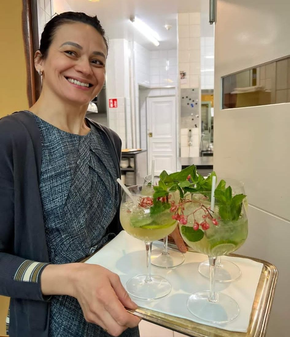 A person holding a tray with two glasses of a green beverage, each garnished with mint leaves and berries.