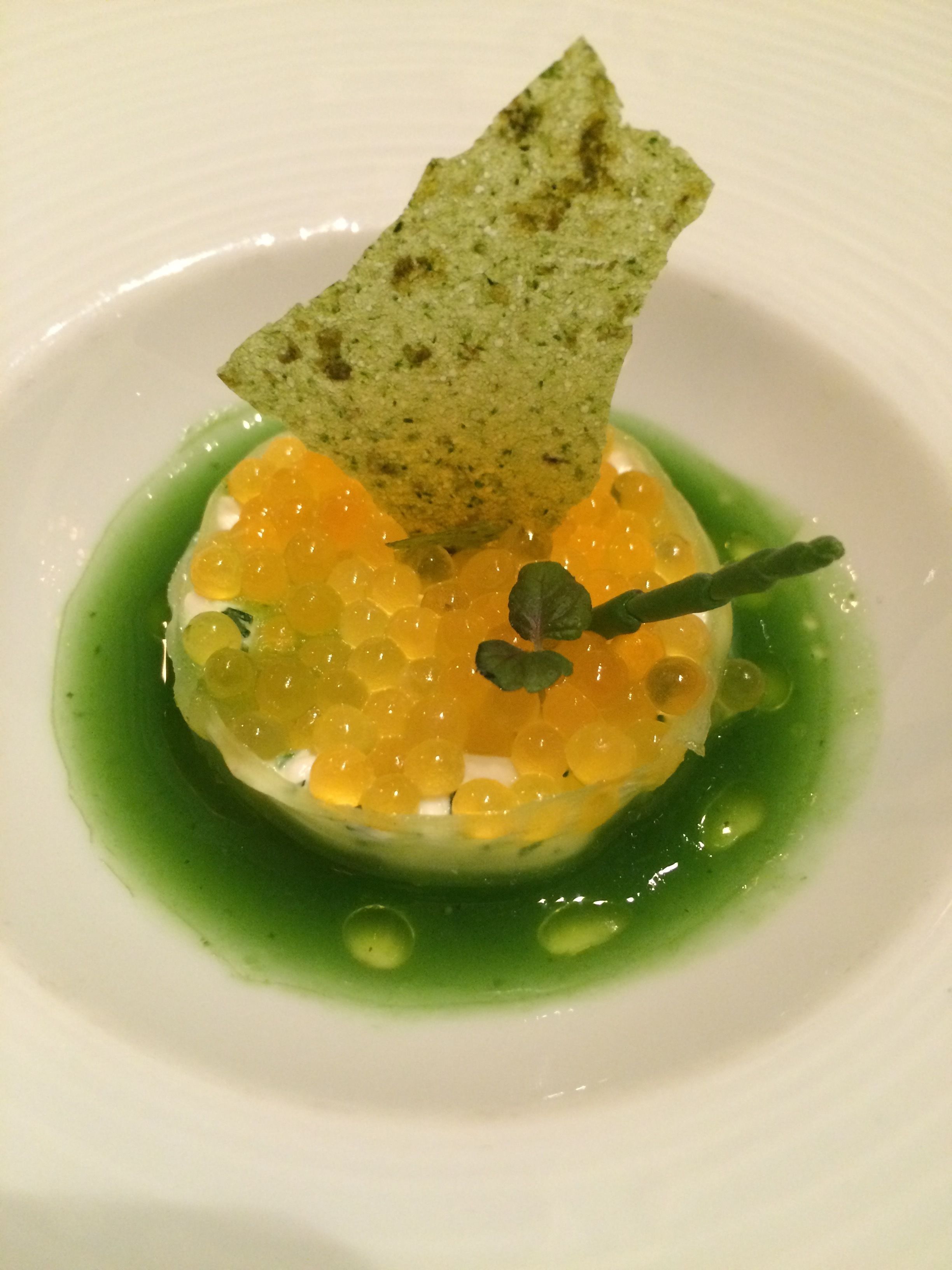 A dish with spherical food items, a green sauce, and a piece of bread on a white plate.