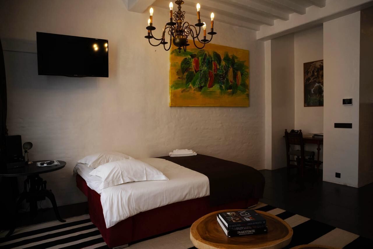 Quarto com cama, televisão, quadro e mesa com livros.