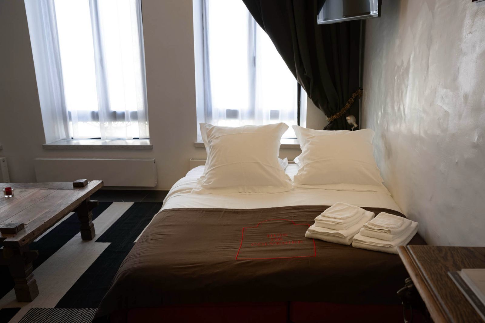 Una habitación de hotel con una cama, una mesita y un ventanal con cortinas.