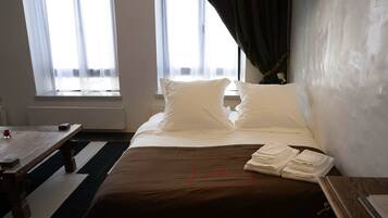 Una habitación de hotel con una cama, una mesita y un ventanal con cortinas.