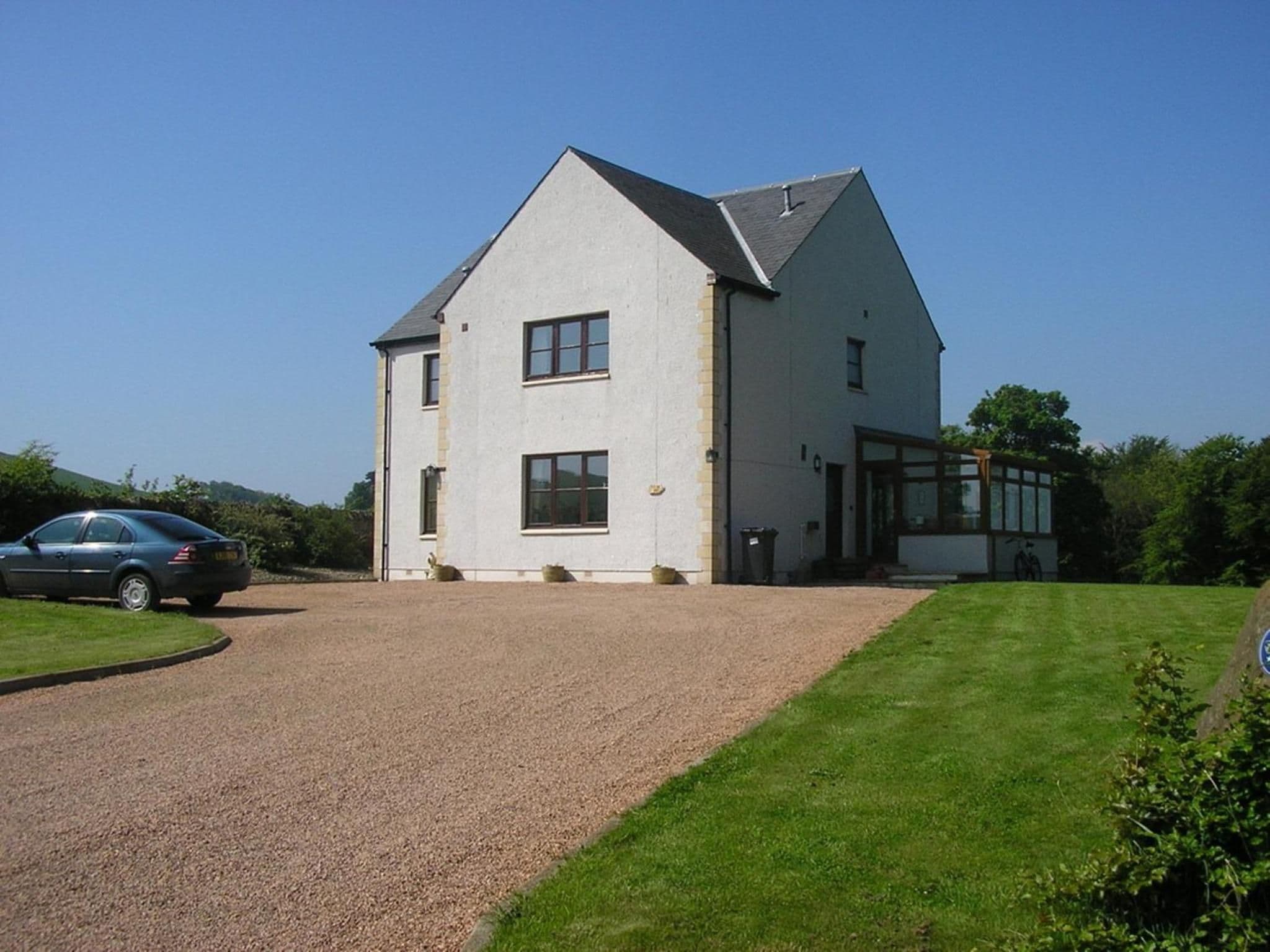 A two-story house with a gravel driveway and a car parked on the left.