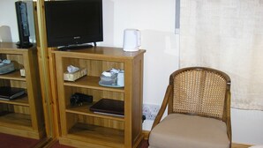 A hotel room with a wooden TV stand, a flat-screen TV, a white coffee maker, a wicker chair, and a mirror. - Balhousie Farm (Leven)
