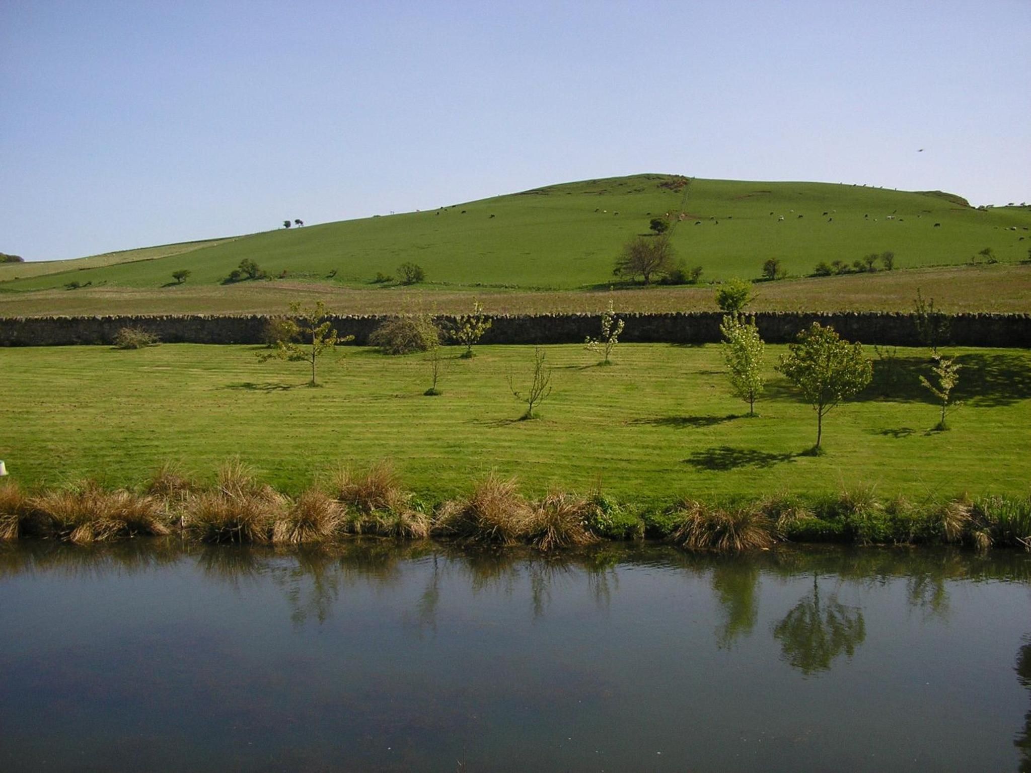 Un paisaje tranquilo con una colina, una masa de agua y vegetación escasa.
