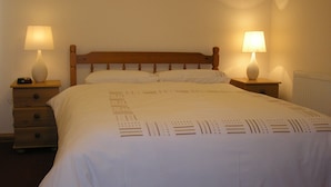 A neatly made bed with a wooden headboard, two bedside tables with lamps, and a radiator on the wall. - Balhousie Farm (Leven)