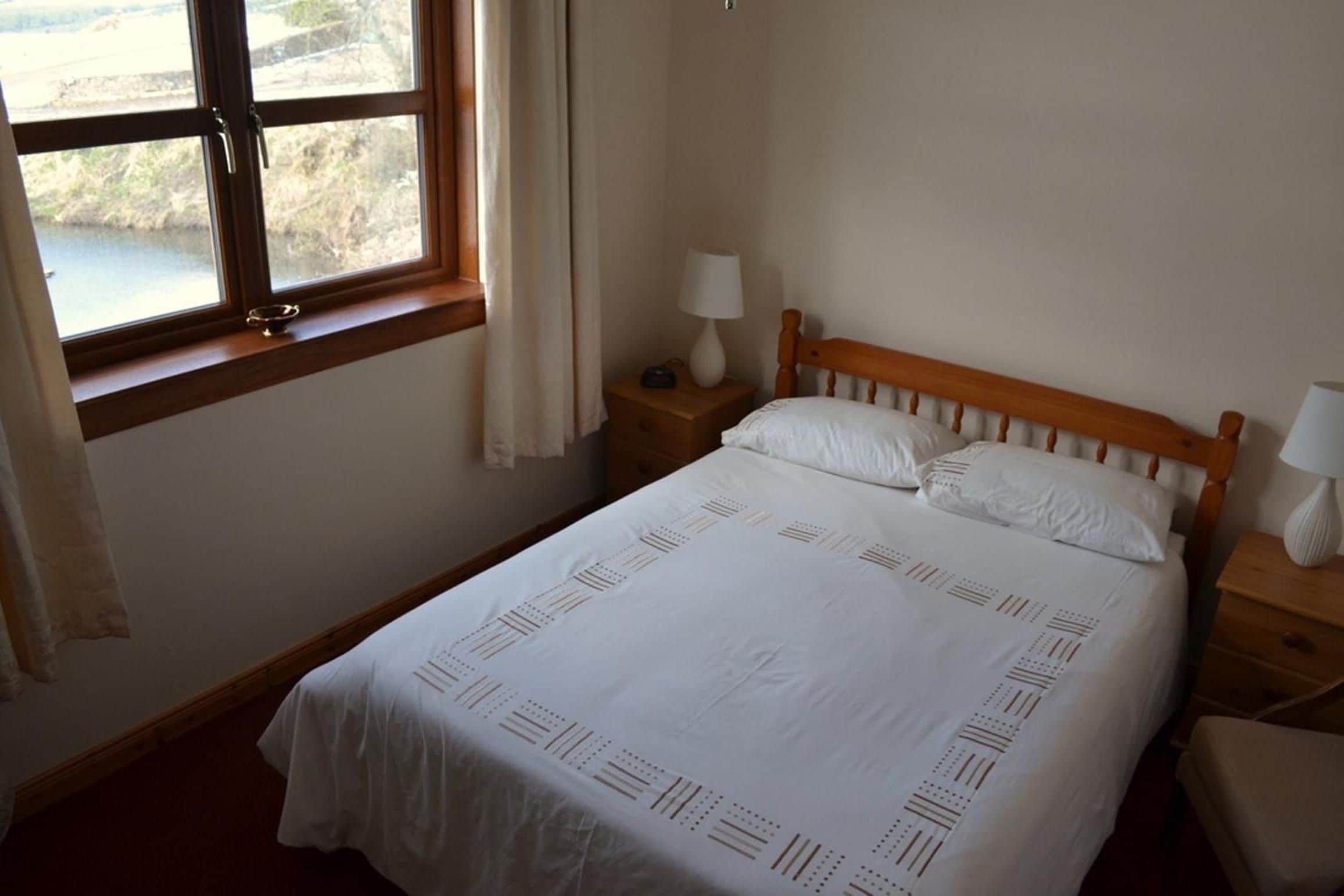 Une chambre à coucher avec un lit, deux tables de chevet, une fenêtre avec des rideaux et une vue sur l’extérieur.