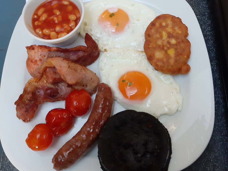 Un plato de comida para el desayuno con huevos, tocino, salchichas, tomates y morcilla.