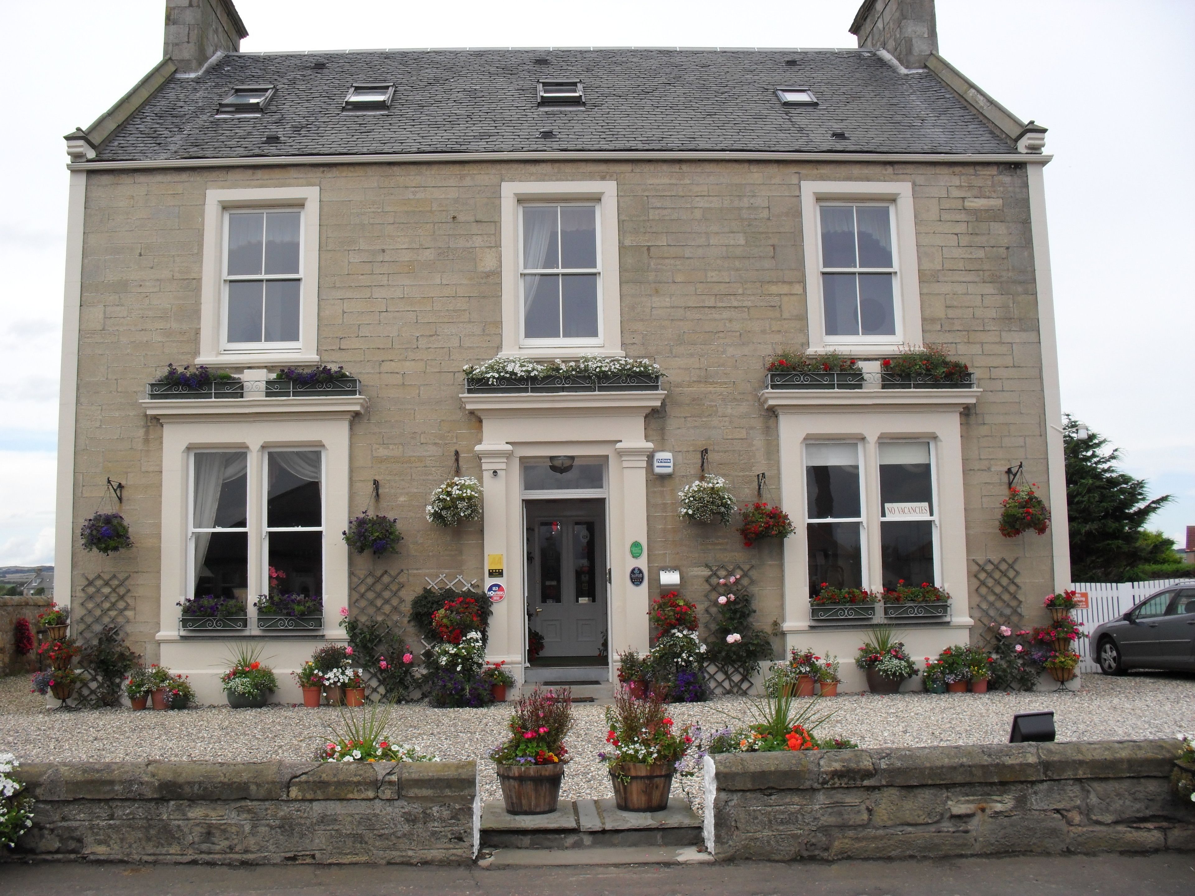 A two-story building with a traditional stone facade, multiple windows, and a variety of potted plants in front.