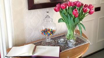 A wooden table with a book, a glass jar of colorful candies, a vase of red tulips, and a framed painting on the wall.