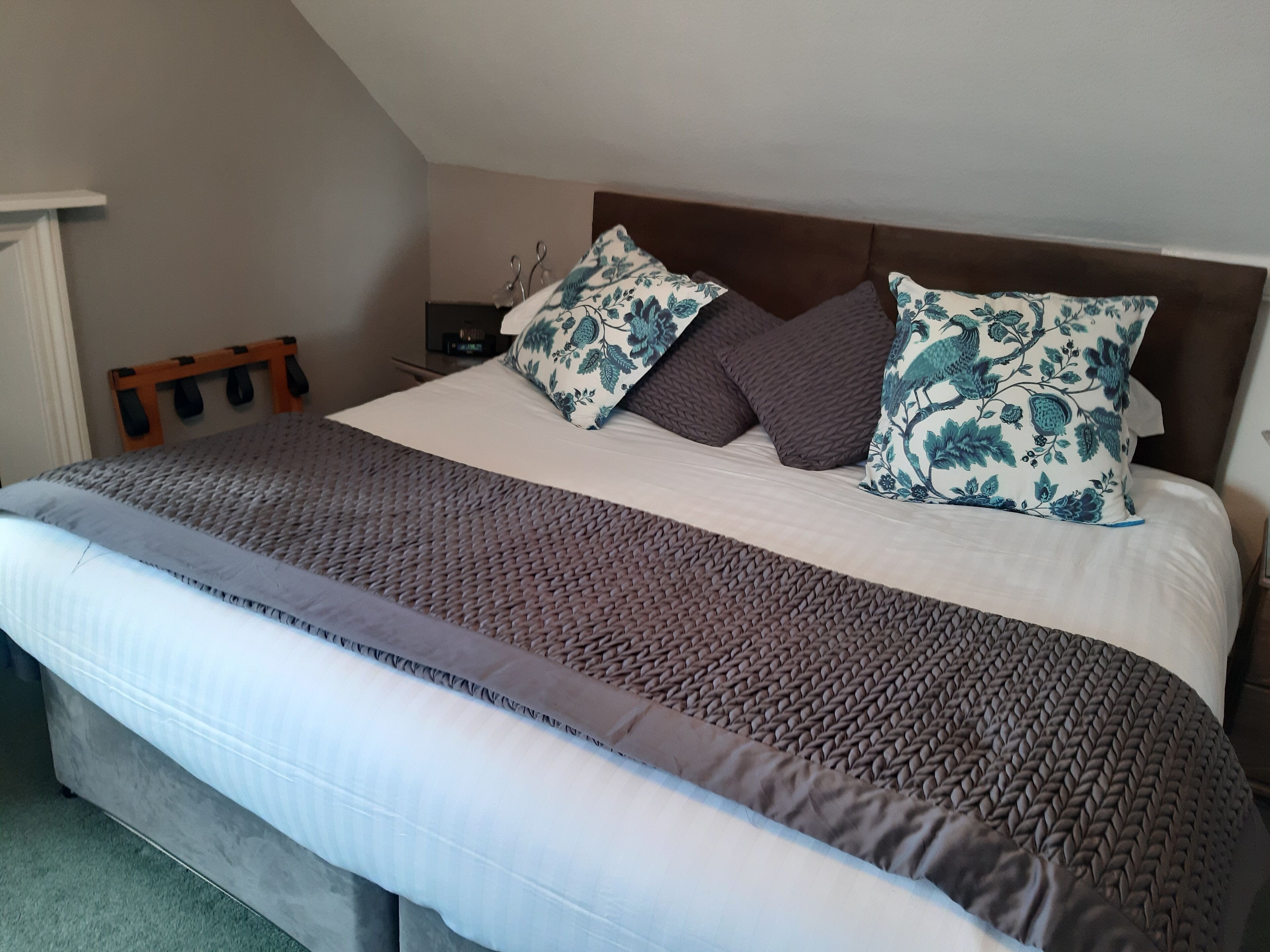 Una cama bien hecha con un edredón marrón y blanco estampado, dos almohadas decorativas con diseño floral azul, y un cabecero de madera.